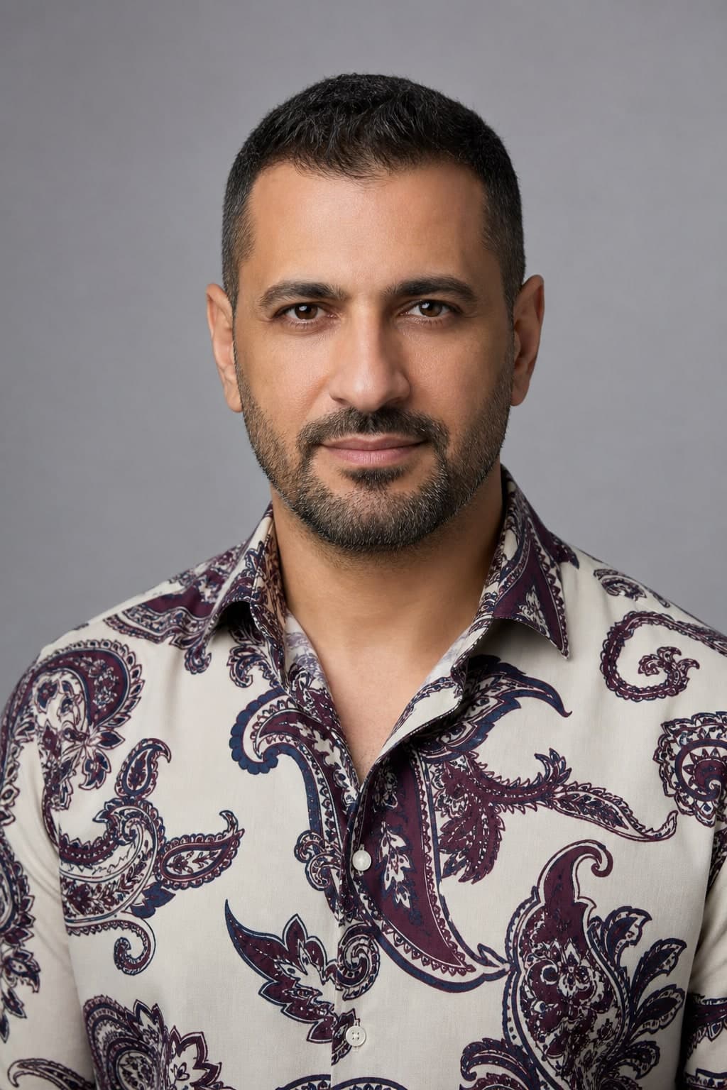 A professional man in a cream shirt with a large burgundy and navy paisley print against a grey studio background.