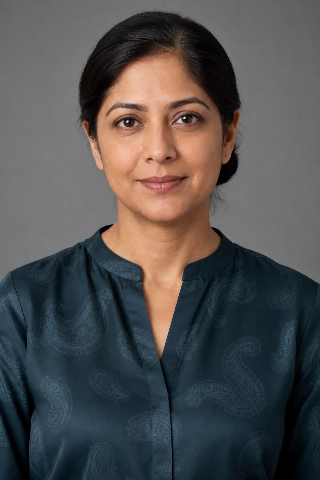 A professional woman in a dark teal blouse with a large tonal paisley pattern against a grey studio background.