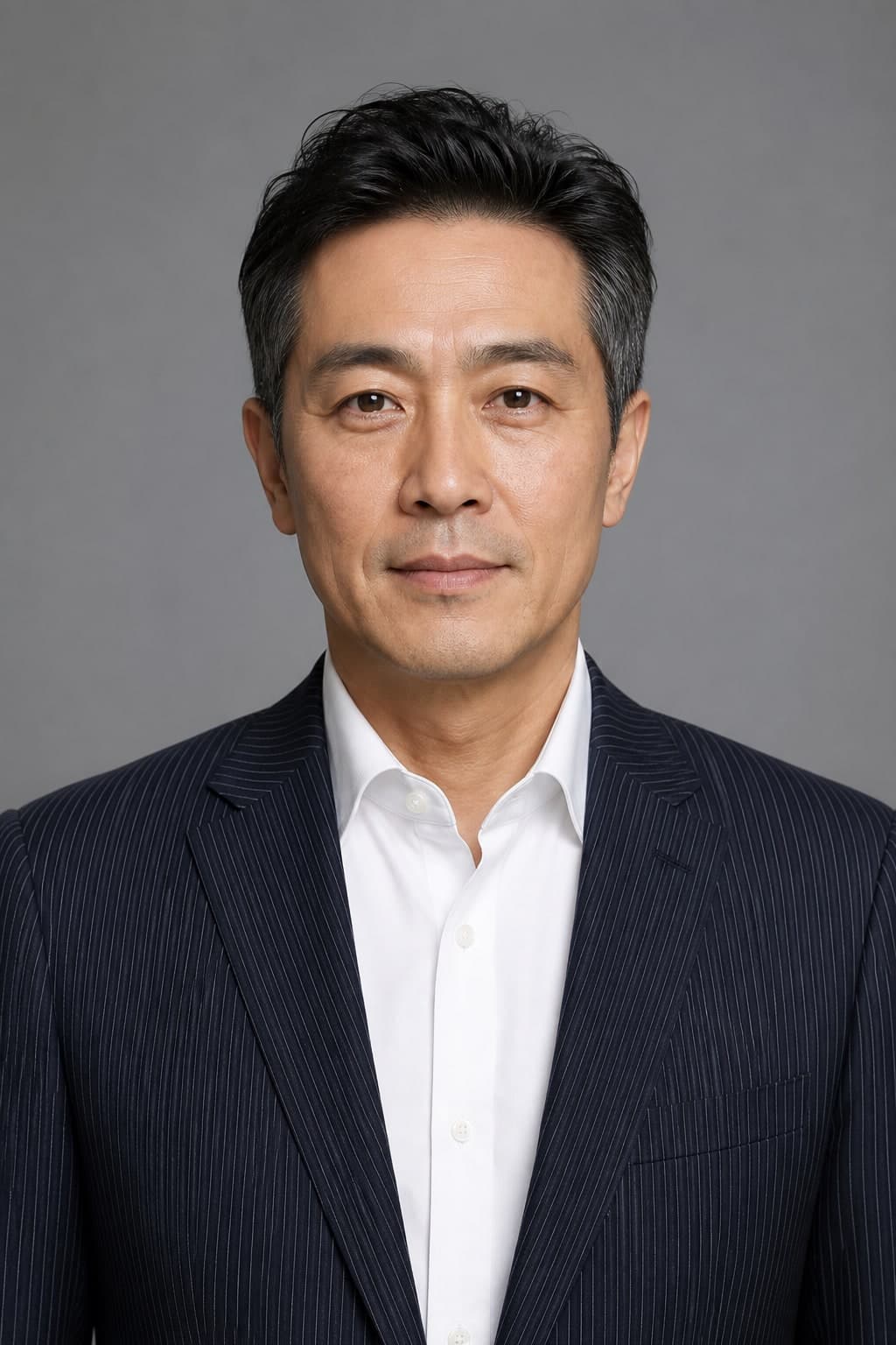 A professional man in a navy jacket with very fine bright pinstripes against a grey studio background.