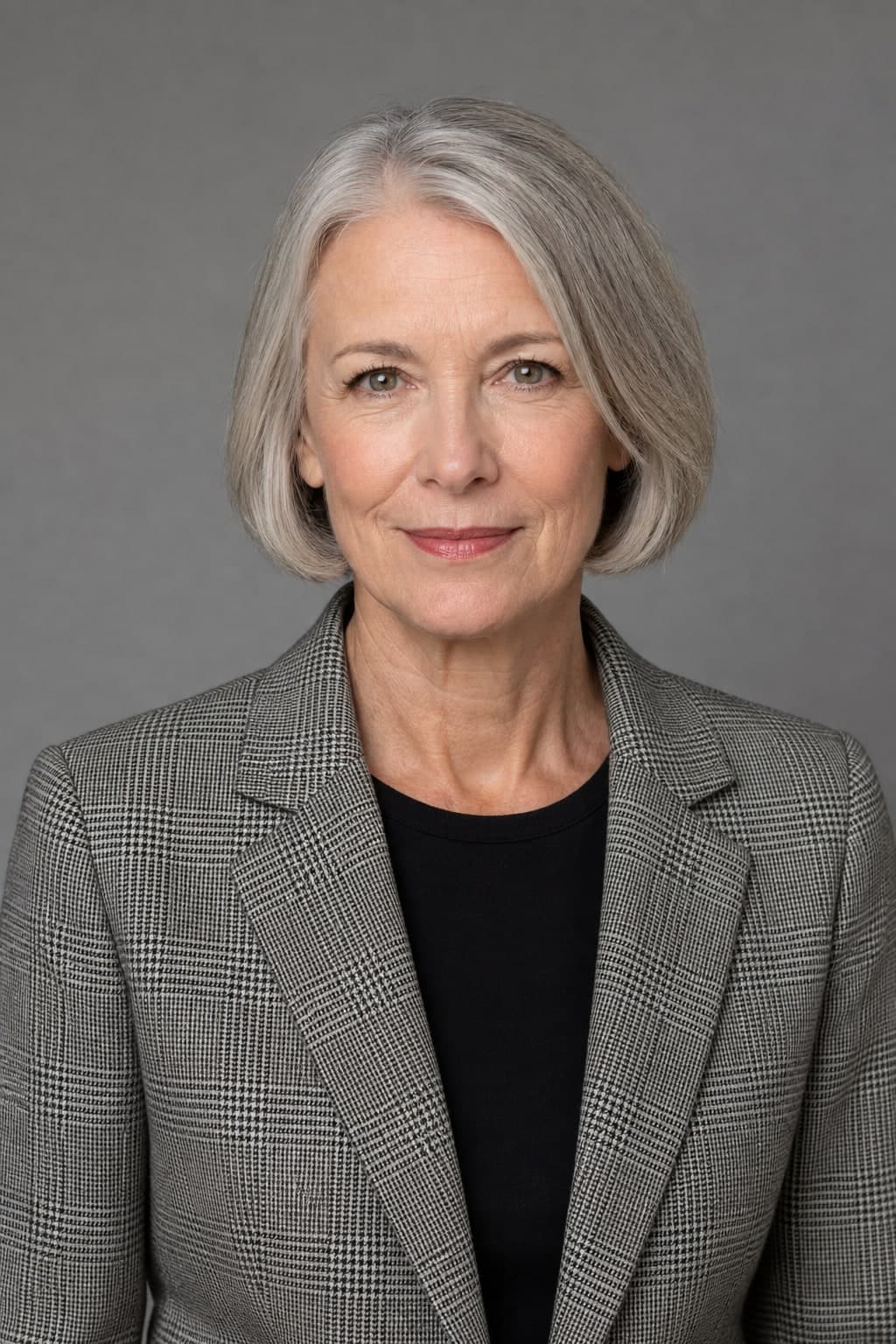 A professional woman in a grey Prince of Wales check jacket against a grey studio background.