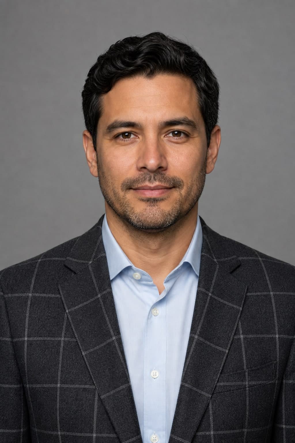 A professional man in a charcoal jacket with a widely spaced windowpane check against a grey studio background.