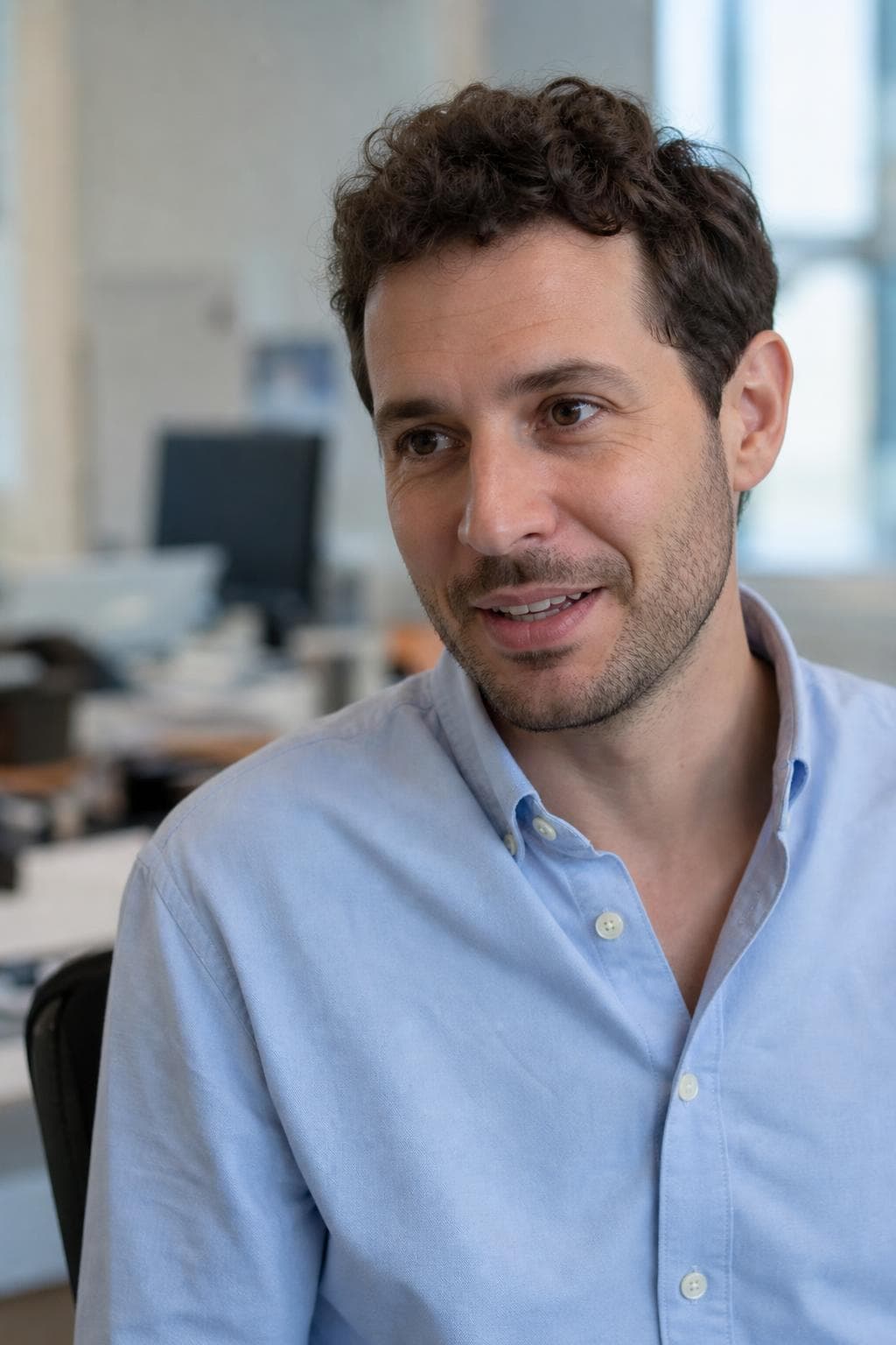 AI profile picture in Slack and Teams style — man in an open-collar blue oxford, his own desk blurred behind him